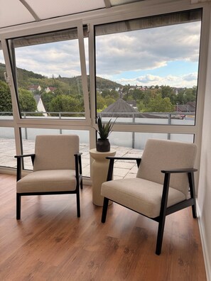 Ein Zimmer mit zwei Stühlen, einer Topfpflanze und Blick auf einen See und Häuser.
