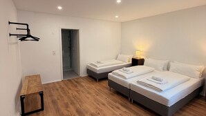 Un dormitorio moderno con dos camas, un banco de madera y un pasillo que conduce a un baño.