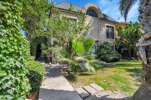 A house with a paved pathway leading to the entrance, surrounded by lush greenery and a palm tree. - Spacious 2BR/2.5BA Coastal Retreat- Parking, Walkable to Water, Near Highways (Los Angeles)