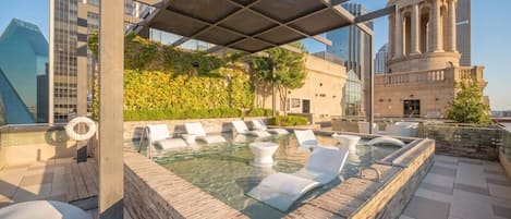 A rooftop pool area with lounge chairs and a clear view of the city skyline.