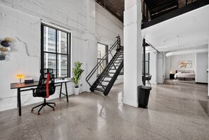 Ein geräumiger Loft mit hoher Decke, freiliegenden Backsteinwänden, einer Treppe und einem großen Fenster für natürliches Licht.