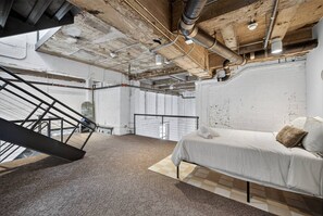 Un dormitorio con cama, una escalera y conductos expuestos.