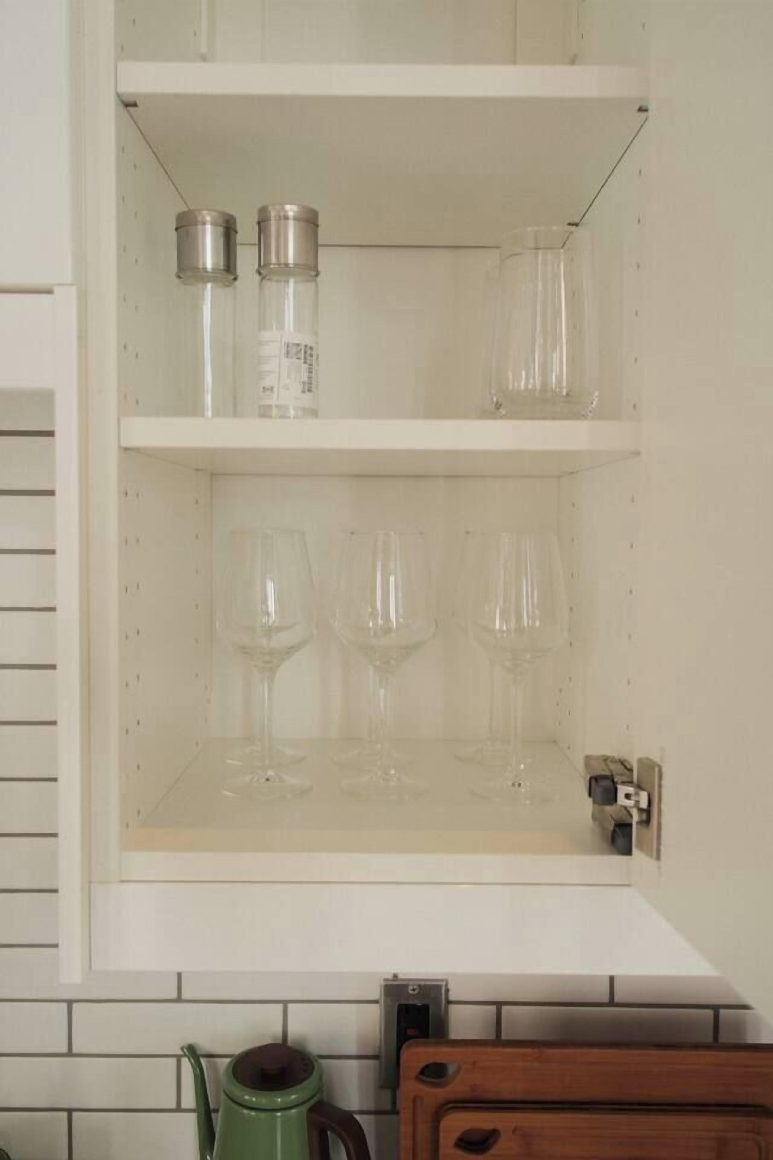 A kitchen with white cabinets, a green kettle, and a wooden cutting board.