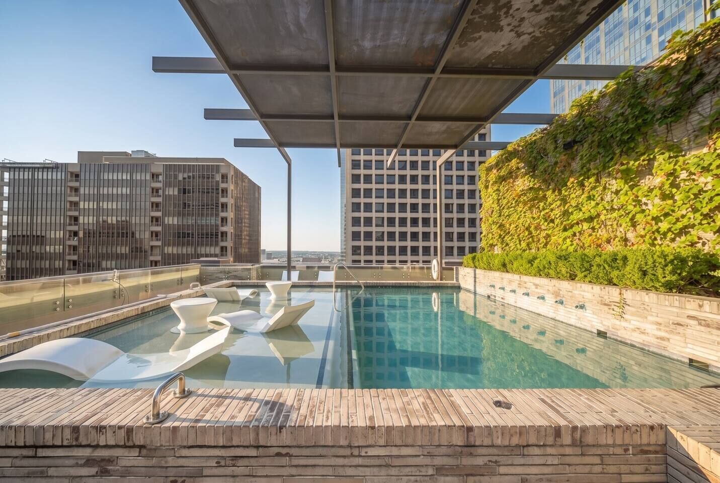 A rooftop pool with a clear view of the cityscape, surrounded by modern buildings and a wooden deck.