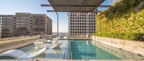 A rooftop pool with a clear view of the cityscape, surrounded by modern buildings and a wooden deck.