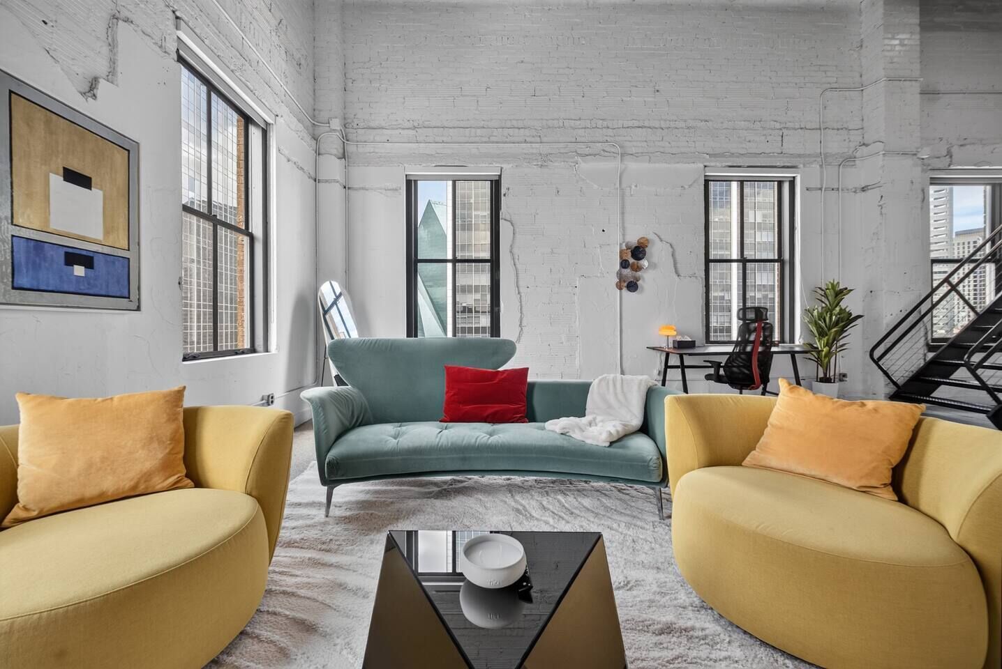 A modern living room with a sofa, two armchairs, a coffee table, and a staircase.