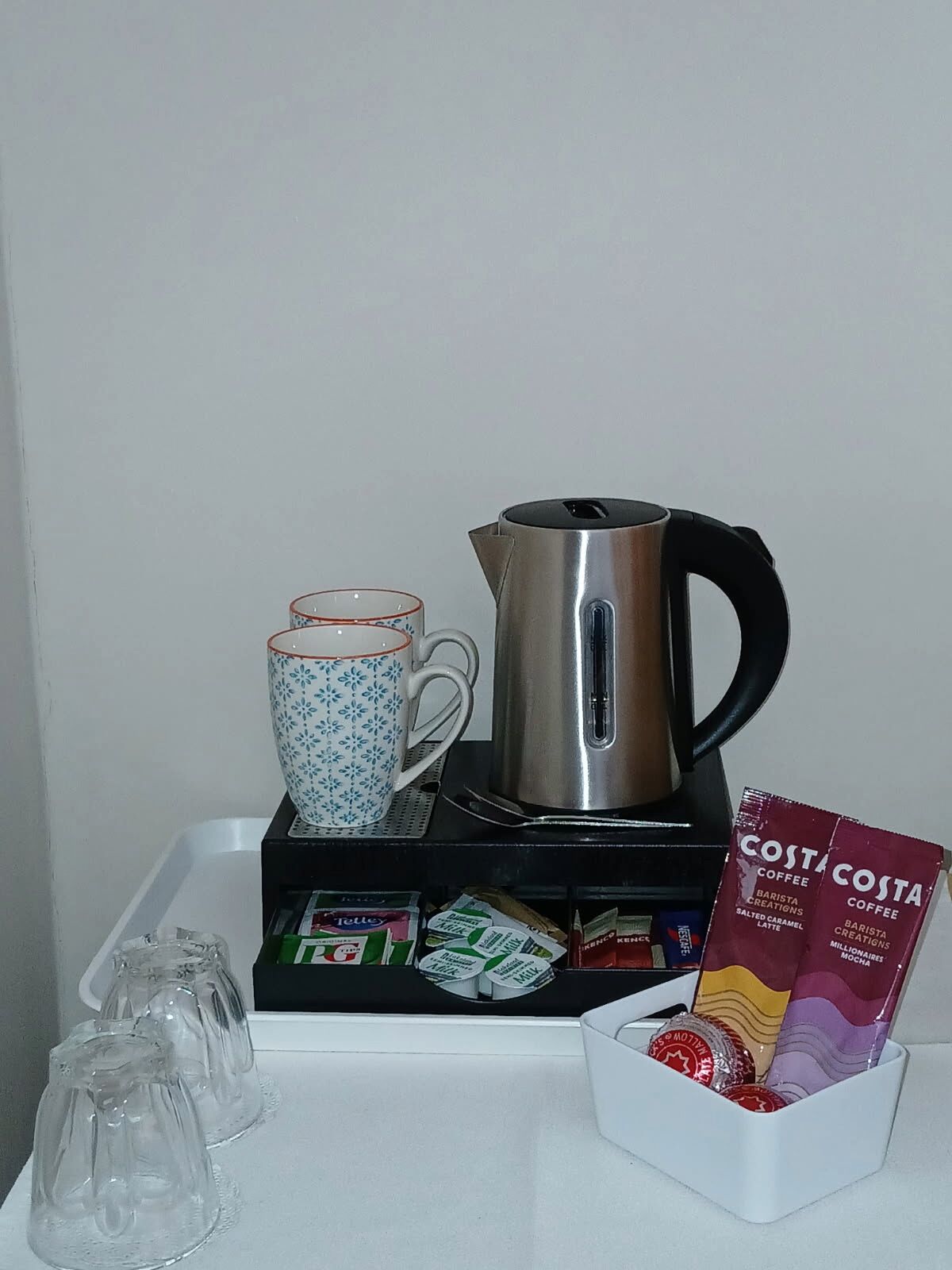 A coffee station with a coffee maker, cups, and coffee packets.