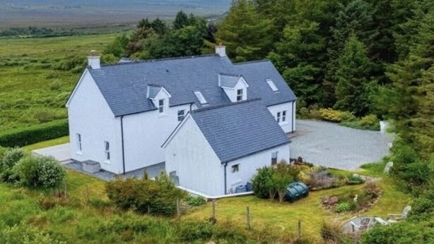 A two-story house with a sloped roof, surrounded by greenery and a clear sky. - Larchside Guest House  (Portree)