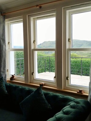 A room with a green sofa, three windows, and a view of greenery and hills. - Larchside Guest House (Portree)