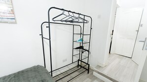 Um porta-roupas de metal com cabides e prateleiras, um tapete cinzento e uma porta branca em um quarto com soalho de madeira clara.