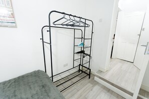 Ein Metalltrockner mit Kleiderbügeln und Ablagen, ein grauer Teppich und eine weiße Tür in einem Raum mit hellem Holzboden.