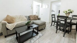 Uma sala de estar moderna com um sofá cinzento, uma mesa de centro e um espaço de jantar com mesa e cadeiras.