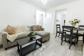 Ein modernes Wohnzimmer mit grauem Sofa, einem Couchtisch und einem Essbereich mit Tisch und Stühlen.