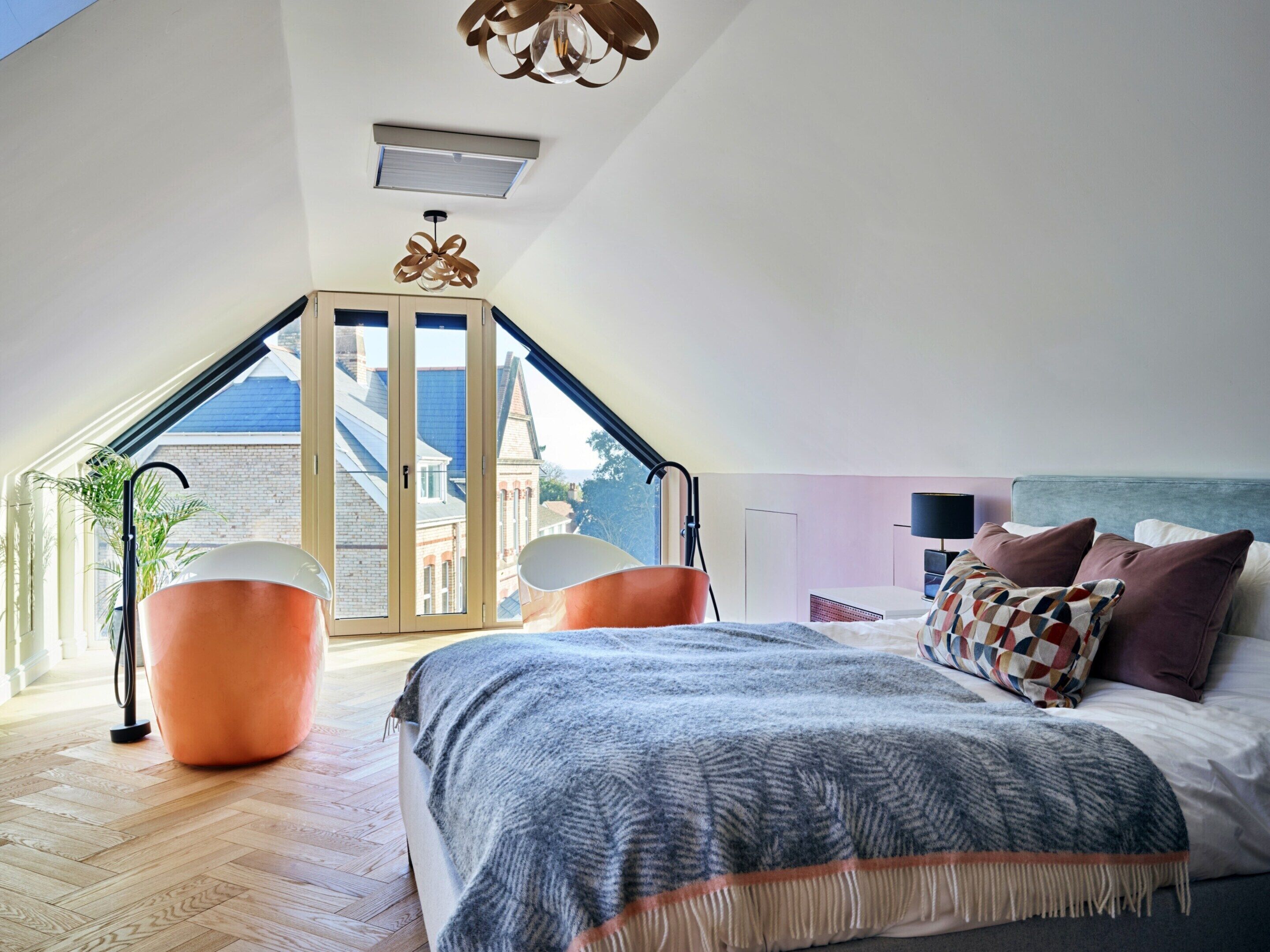 A bedroom with a sloped ceiling, a bed with a patterned blanket, two side tables, and a view through a glass door.