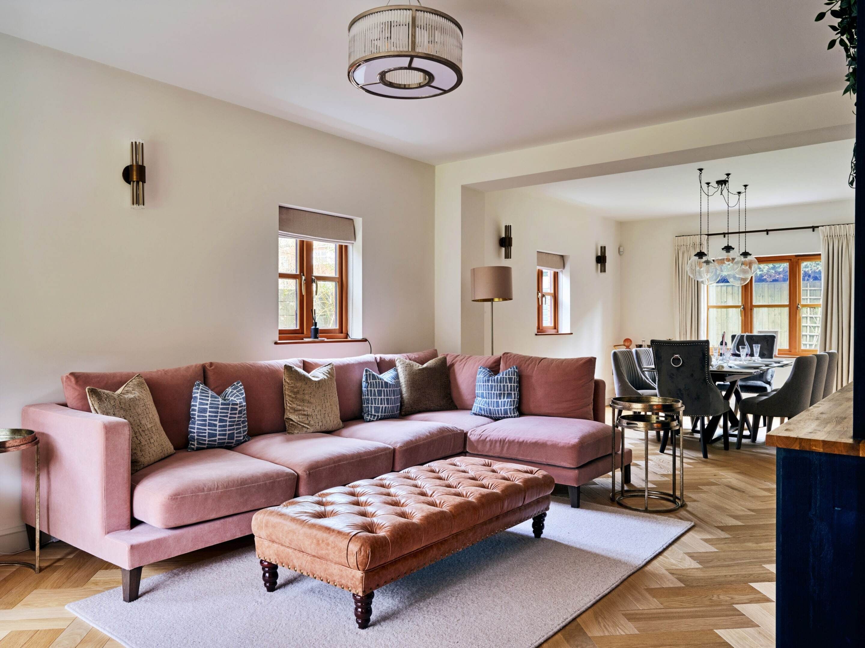 A living room with a pink sofa, a tufted ottoman, and a dining area with a table and chairs.