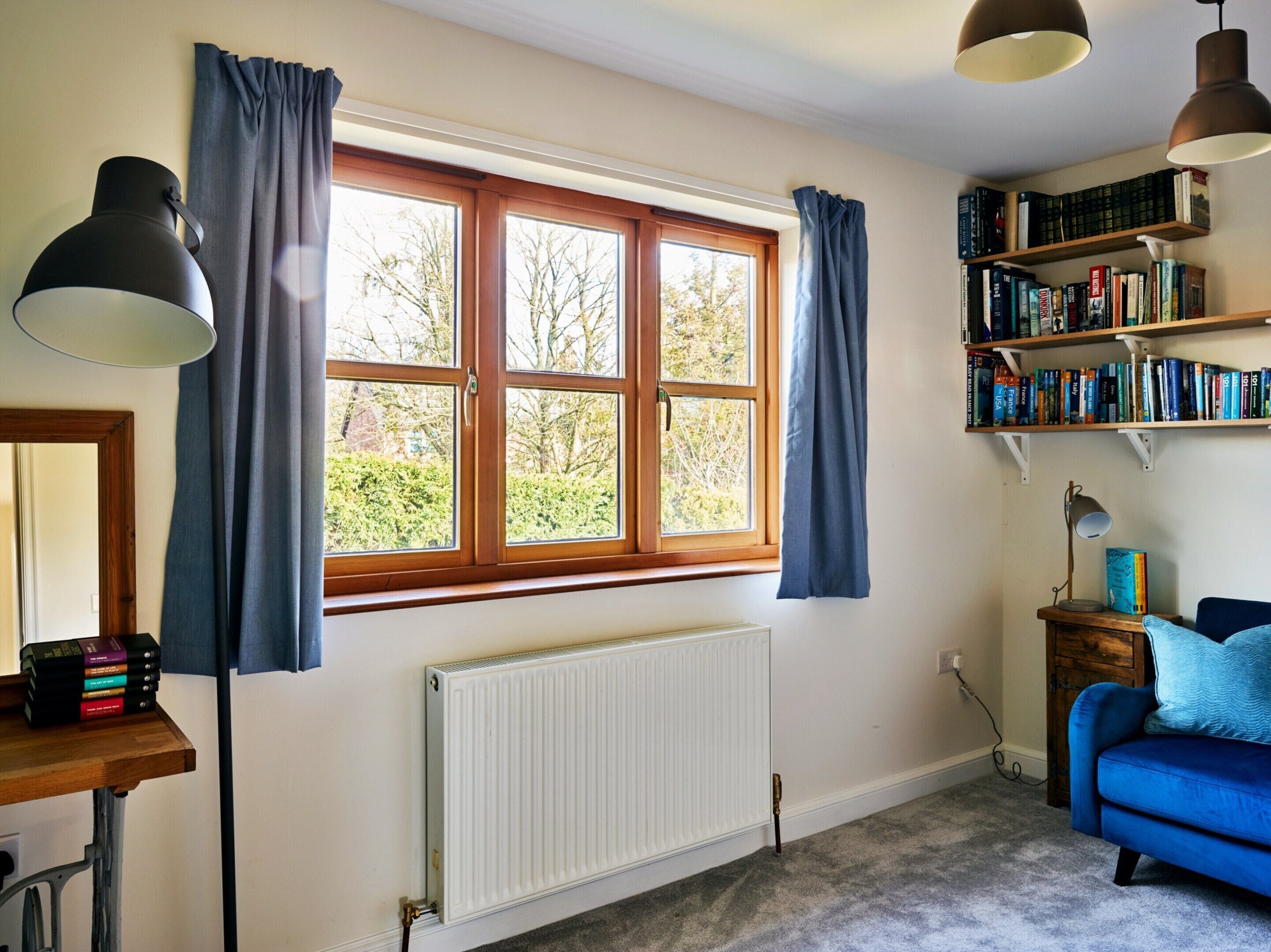 A room with a large window, a radiator, a bookshelf, a desk with books, and a blue sofa.