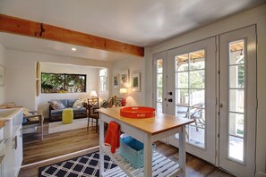 Un interior bien iluminado con techo de madera, una zona de comedor con mesa y sillas, un sofá y una cocina con pileta y encimera.