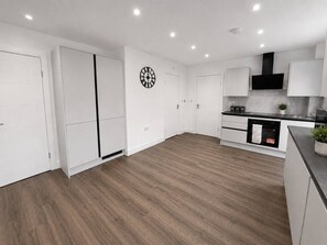 A modern kitchen with white cabinetry, a built-in oven, and a clock on the wall. - The Hayloft • 4 Bedroom 4 Bathroom • New Build House • Sleeps 7 • Driveway Parking • Yoko Property (Huntingdon)