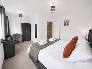 A hotel room with a bed, a desk, a wardrobe, and a bathroom door. - The Hayloft • 4 Bedroom 4 Bathroom • New Build House • Sleeps 7 • Driveway Parking • Yoko Property (Huntingdon)