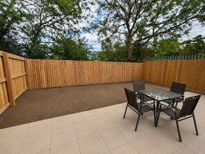 An outdoor patio area with a wooden fence, a tiled floor, and a table with chairs. - The Hayloft • 4 Bedroom 4 Bathroom • New Build House • Sleeps 7 • Driveway Parking • Yoko Property (Huntingdon)