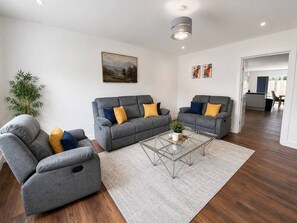 A modern living room with a grey sofa set, a glass coffee table, and a large painting on the wall. - The Hayloft • 4 Bedroom 4 Bathroom • New Build House • Sleeps 7 • Driveway Parking • Yoko Property (Huntingdon)