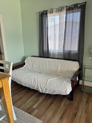 Ein Zimmer mit Holzboden, einem weißen Sofa, einem kleinen Tisch und einem Fenster mit Vorhängen.