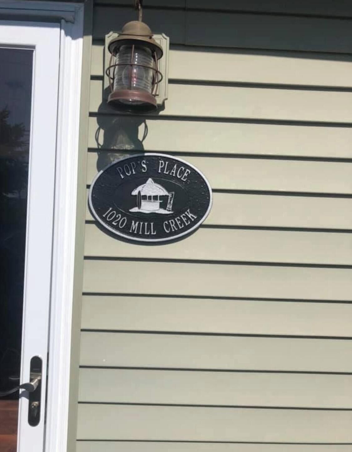 Ett husnummer med texten ”Pop’s Place” och adressen ”1020 Mill Creek” på en beige fasadvägg.