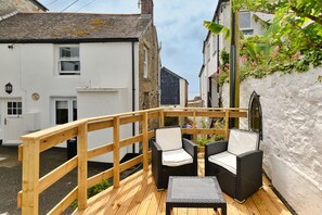 A wooden deck with wicker furniture and a small table, overlooking a narrow street with white buildings. - Grand Devon Country House for 15 (Penzance)