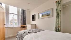 Ein Schlafzimmer mit Bett, Fenster, Schreibtisch und einem gerahmten Bild an der Wand.