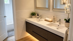 A modern bathroom with a double sink, two mirrors, a potted plant, a candle, and a towel rack. - Bright Modern Room w/ Balcony Access (Miami)