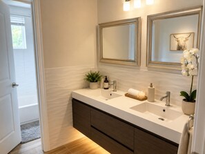 A modern bathroom with a double sink, two mirrors, a potted plant, a candle, and a towel rack. - Bright Modern Room w/ Balcony Access (Miami)