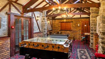 A room with a foosball table, a fireplace, and a stone wall.