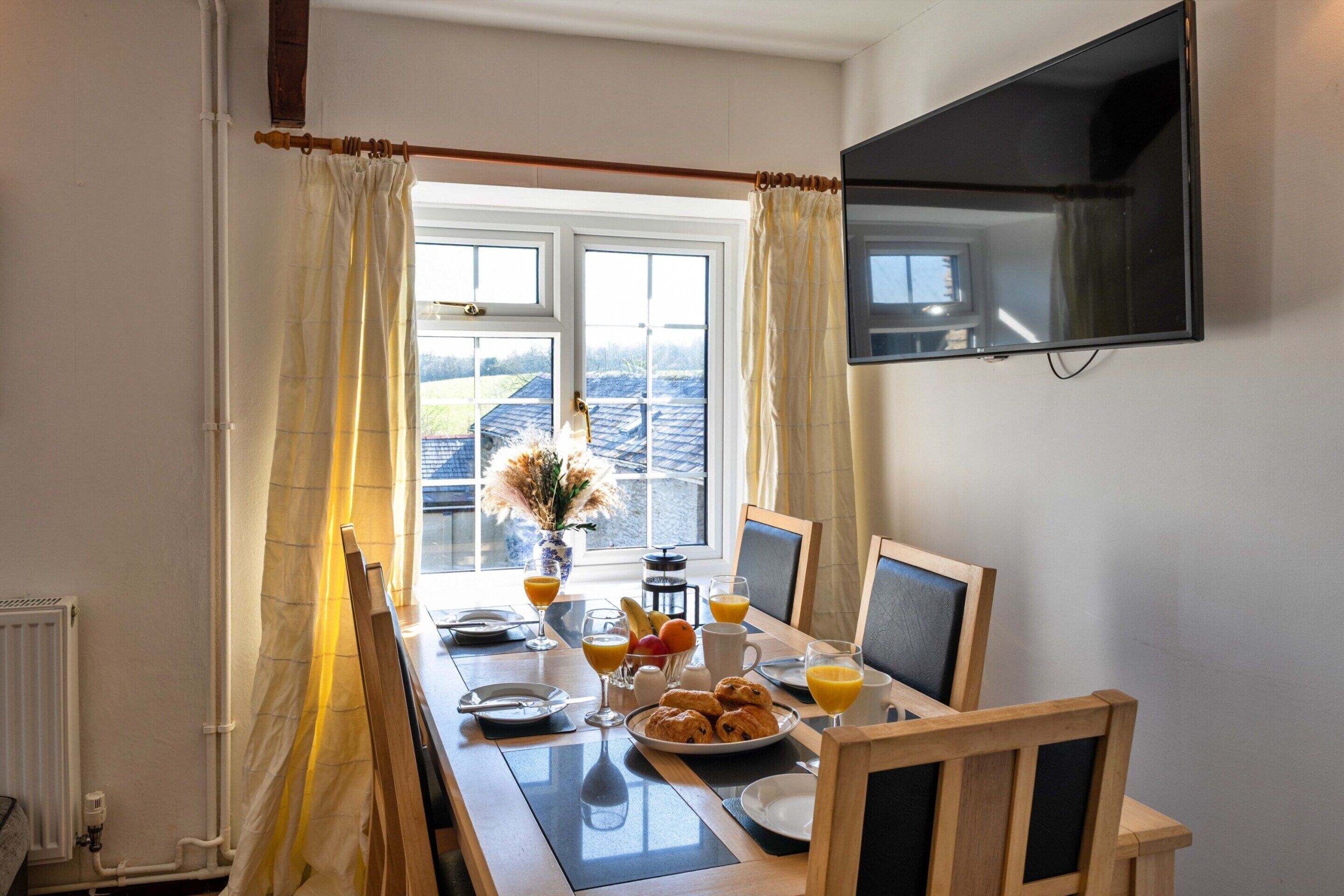 Una mesa de desayuno con un televisor montado en la pared, una ventana con cortinas y un radiador.