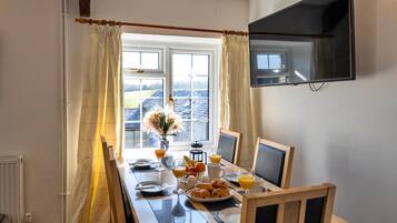 Una mesa de desayuno con un televisor montado en la pared, una ventana con cortinas y un radiador.
