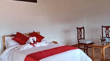 Una cama bien hecha con ropa de cama roja y blanca, suelo de madera, una silla de madera y una mesa con un florero.