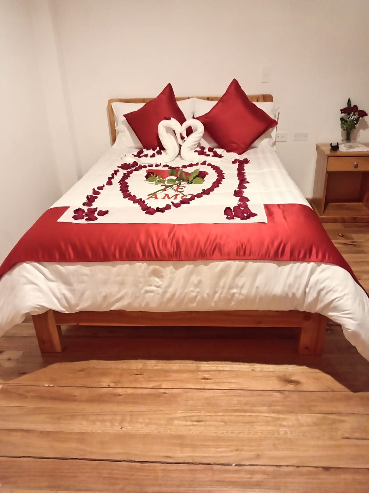 A bed with a heart-shaped decoration made of rose petals and a white pillow.