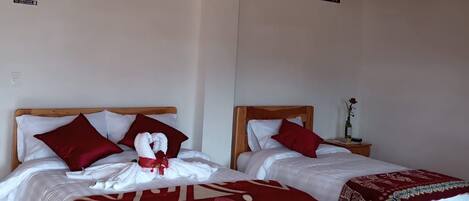 A hotel room with two wooden beds, red and white bedding, wooden flooring, and a wooden ceiling.