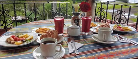 Una mesa dispuesta con alimentos para el desayuno, como croissants, fruta y bebidas, con vistas a un paisaje pintoresco.