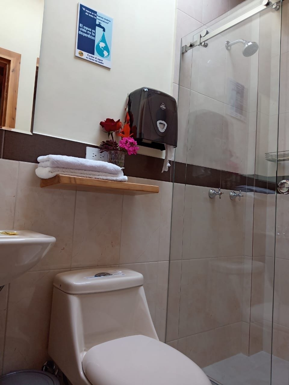 Un baño con inodoro, ducha y estante con toallas y flores.