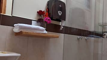 Un baño con inodoro, ducha y estante con toallas y flores.