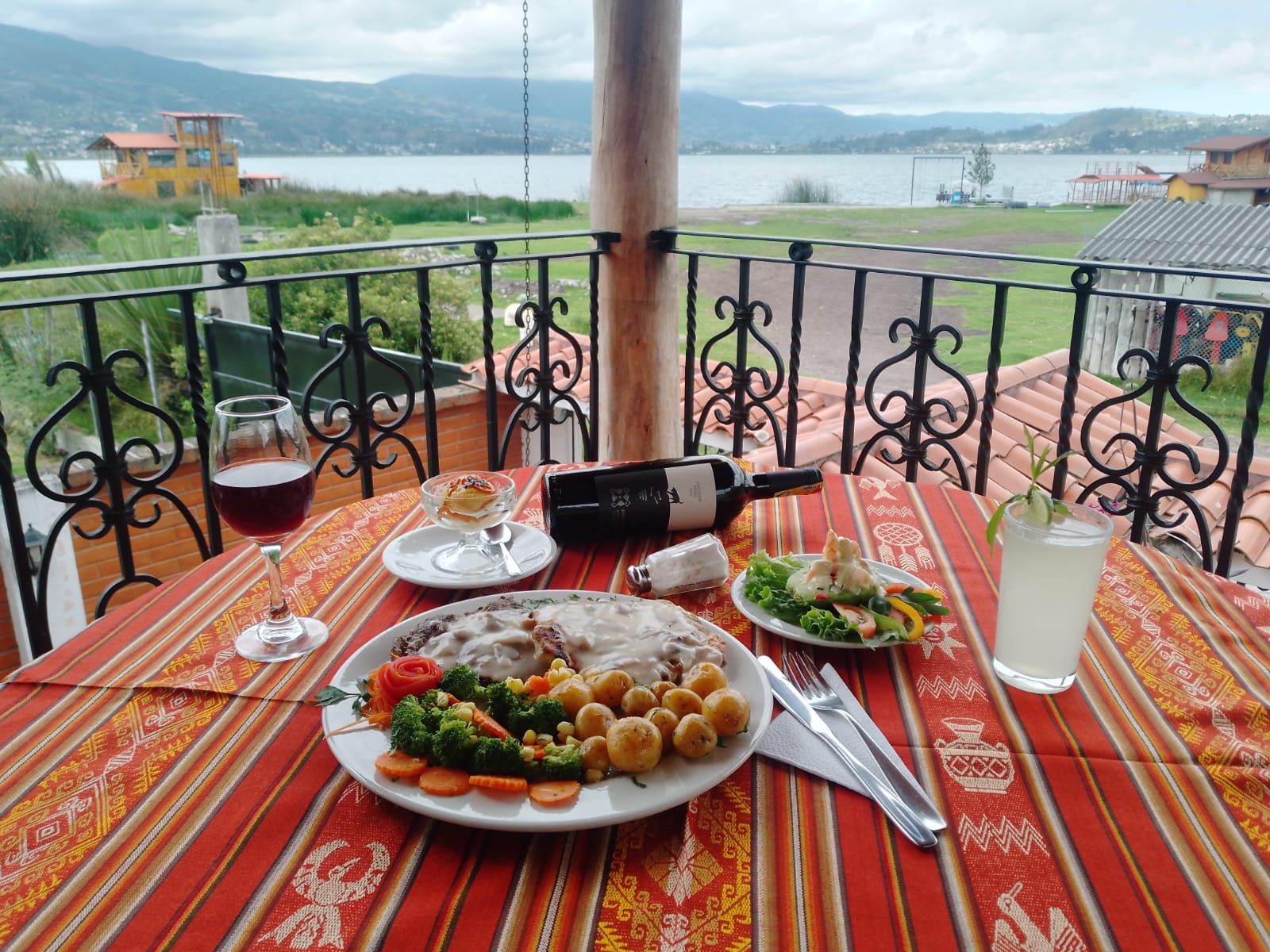 Una mesa de comedor con comida, una botella de vino y vistas a un lago y montañas.