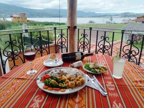 Una mesa de comedor con comida, una botella de vino y vistas a un lago y montañas.