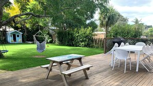 A wooden deck with a picnic table and chairs, surrounded by a lush green lawn and trees. - Relaxing haven for Families - minutes walk to the beach, shops & dining (Tauranga)