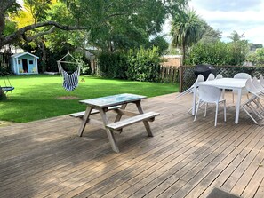 Eine Holzterrasse mit Picknicktisch und Stühlen, umgeben von einem üppigen Rasen und Bäumen.