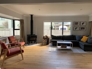 Ein Wohnzimmer mit einer Couch, einem Sessel, einem Kamin und Blick durch ein großes Fenster.