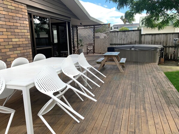 An outdoor patio with a wooden deck, white plastic chairs, and a picnic table. - Relaxing haven for Families - minutes walk to the beach, shops & dining (Tauranga)