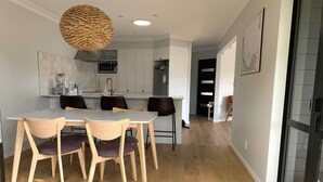 A modern kitchen with white cabinets, a dining table with chairs, and a hanging light fixture. - Relaxing haven for Families - minutes walk to the beach, shops & dining (Tauranga)