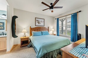 Ein Schlafzimmer mit Bett, Nachttischen, Deckenventilator, einem Fenster mit Vorhängen und einem Wandbild.