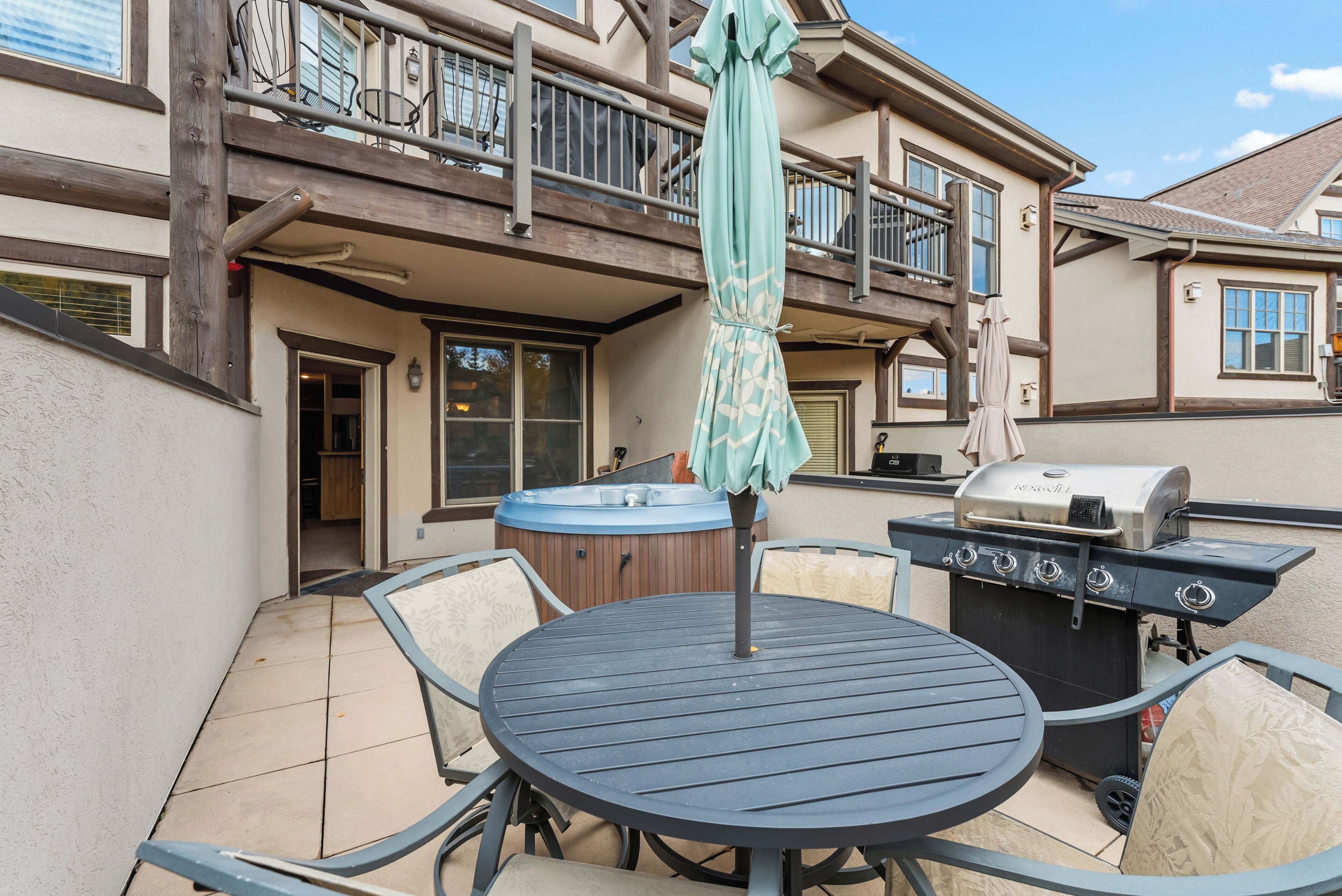Une terrasse extérieure avec une table ronde, des chaises, un barbecue et un jacuzzi.