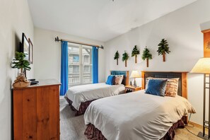 A bedroom with two beds, a dresser, a nightstand, a lamp, and a window with blinds. - Walk to Peak 9, Quicksilver Lift & Main St - Private Hot Tub & Garage (Breckenridge)
